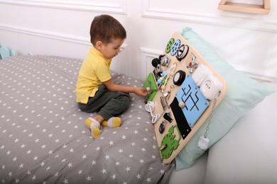 Little boy playing with busy board on bed at home
