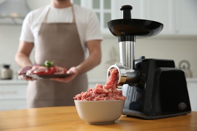 Photo of Closeup view of man with products in kitchen, focus on modern meat grinder