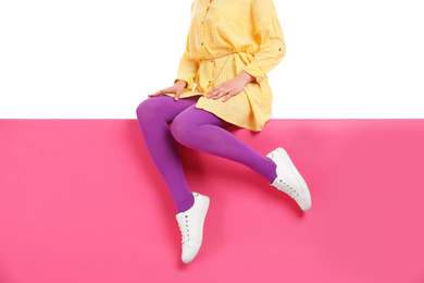 Woman wearing bright tights and stylish shoes sitting on color background, closeup