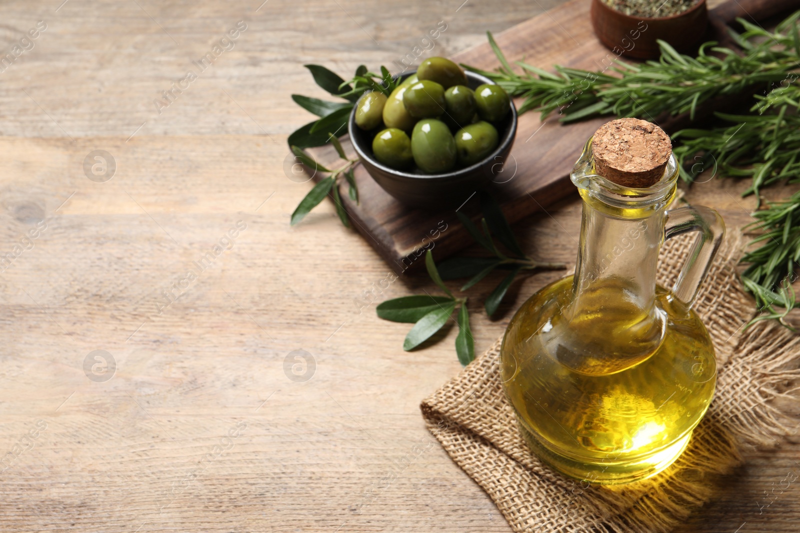 Photo of Glass jug of oil, ripe olives and green leaves on wooden table. Space for text