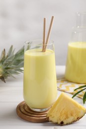 Photo of Tasty pineapple smoothie and fruit on white wooden table