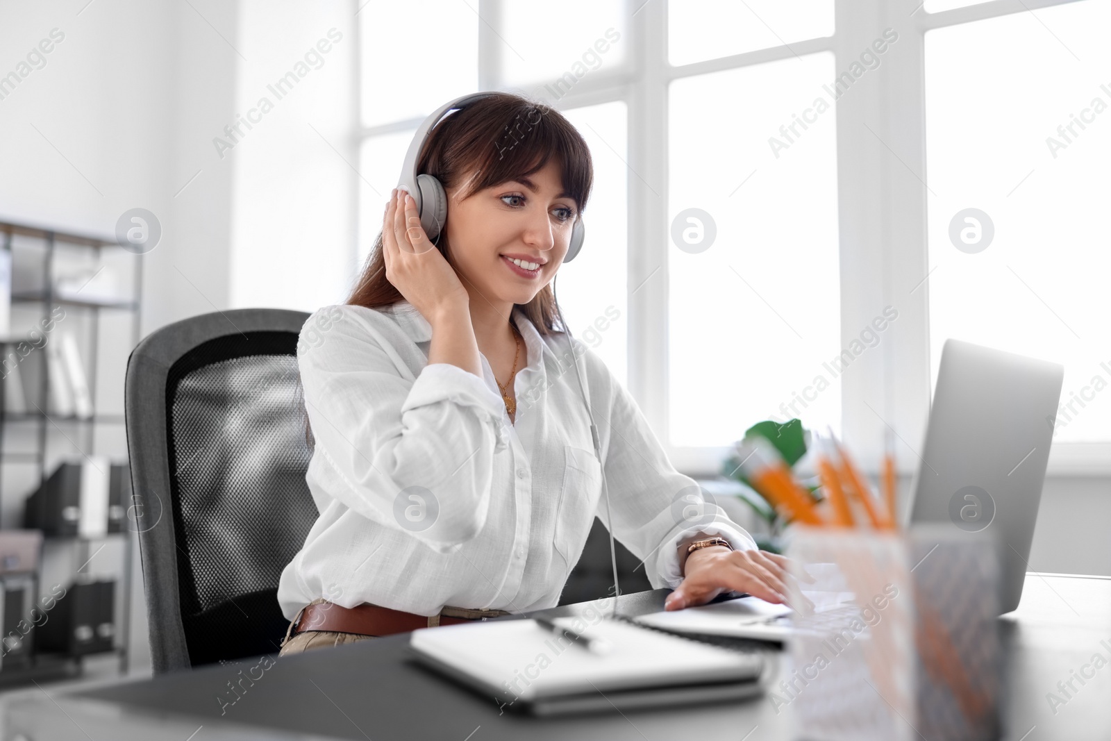 Photo of Woman in headphones watching webinar at table in office