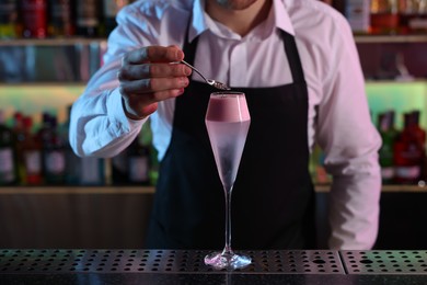 Photo of Bartender decorating fresh alcoholic cocktail with sprinkles at counter in bar, closeup