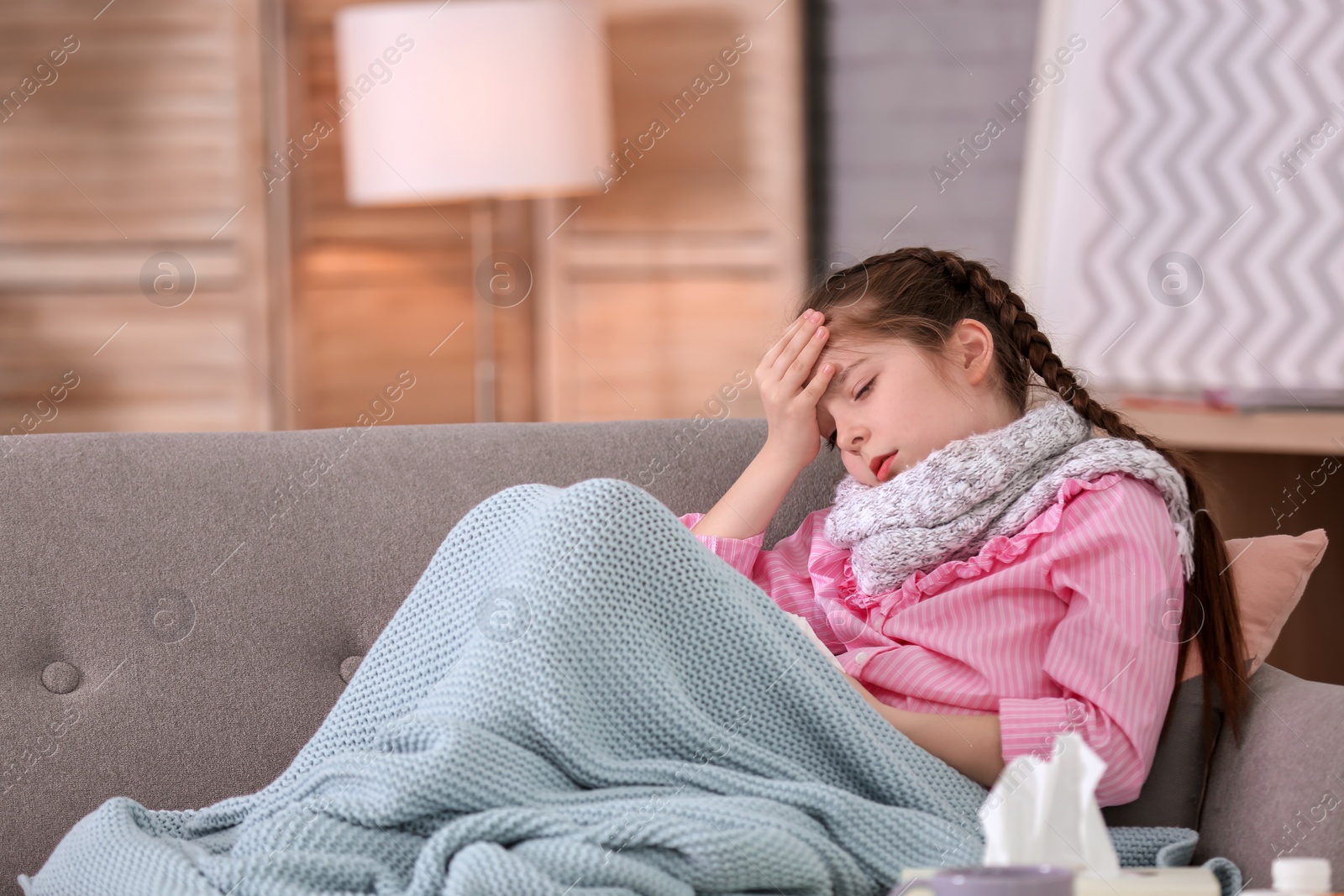 Photo of Little girl with headache suffering from cold on sofa at home