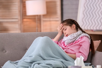 Photo of Little girl with headache suffering from cold on sofa at home