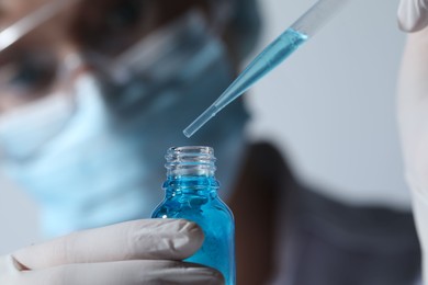 Scientist dripping liquid from pipette into glass bottle on light background, closeup