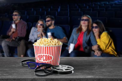 Image of Popcorn, 3D glasses, movie reel on table and young people in cinema hall