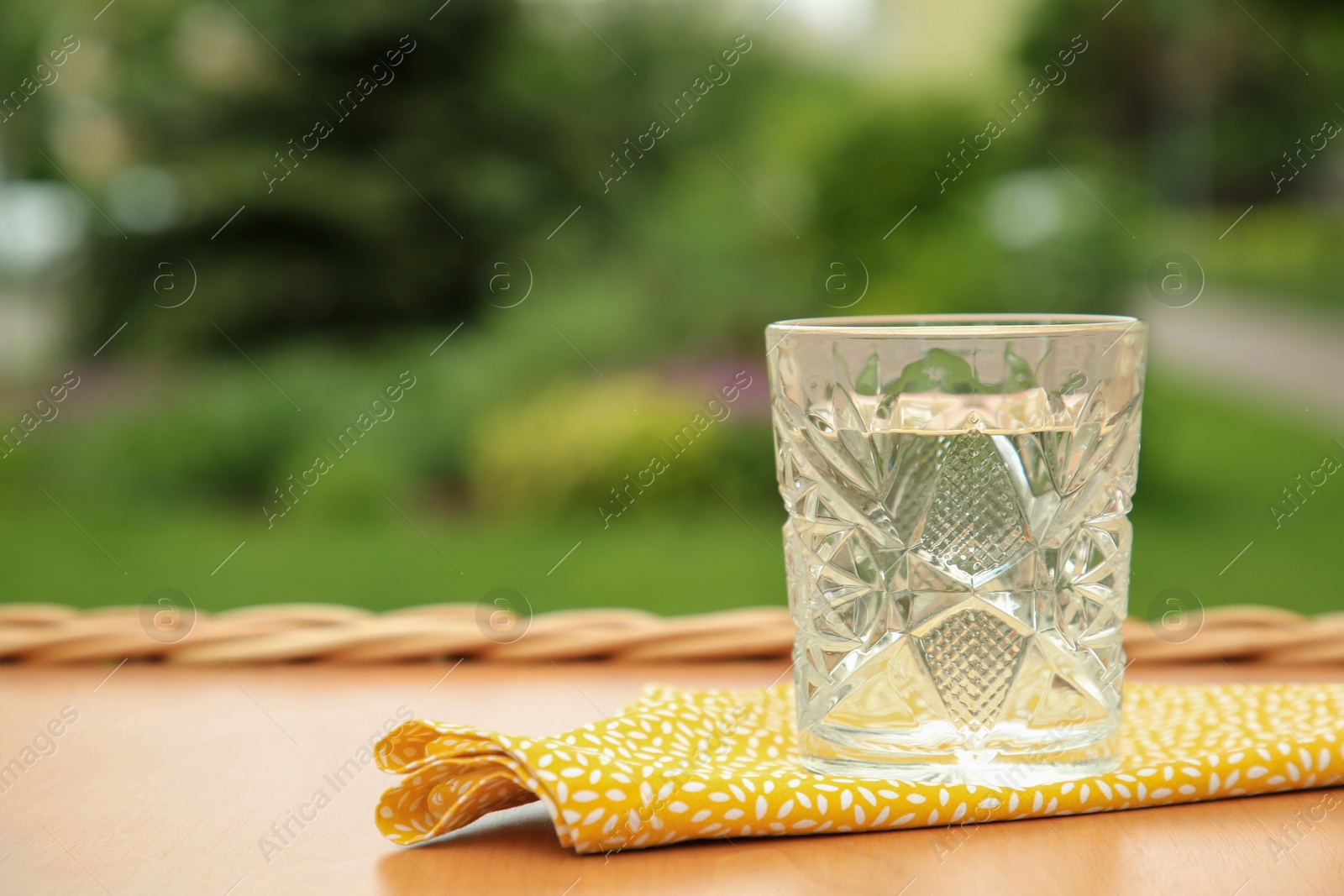 Photo of Glass of fresh water on wooden table outdoors, space for text