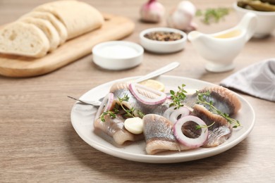 Photo of Plate with delicious salted herring fillets, garlic, thyme and onion rings on wooden table