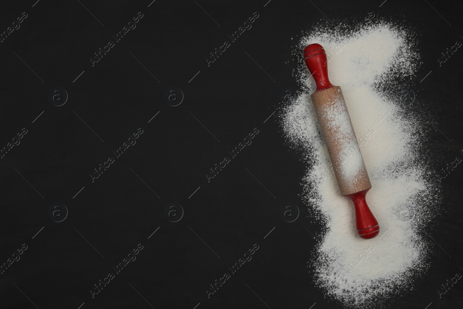 Photo of Flour and rolling pin on black table, top view. Space for text