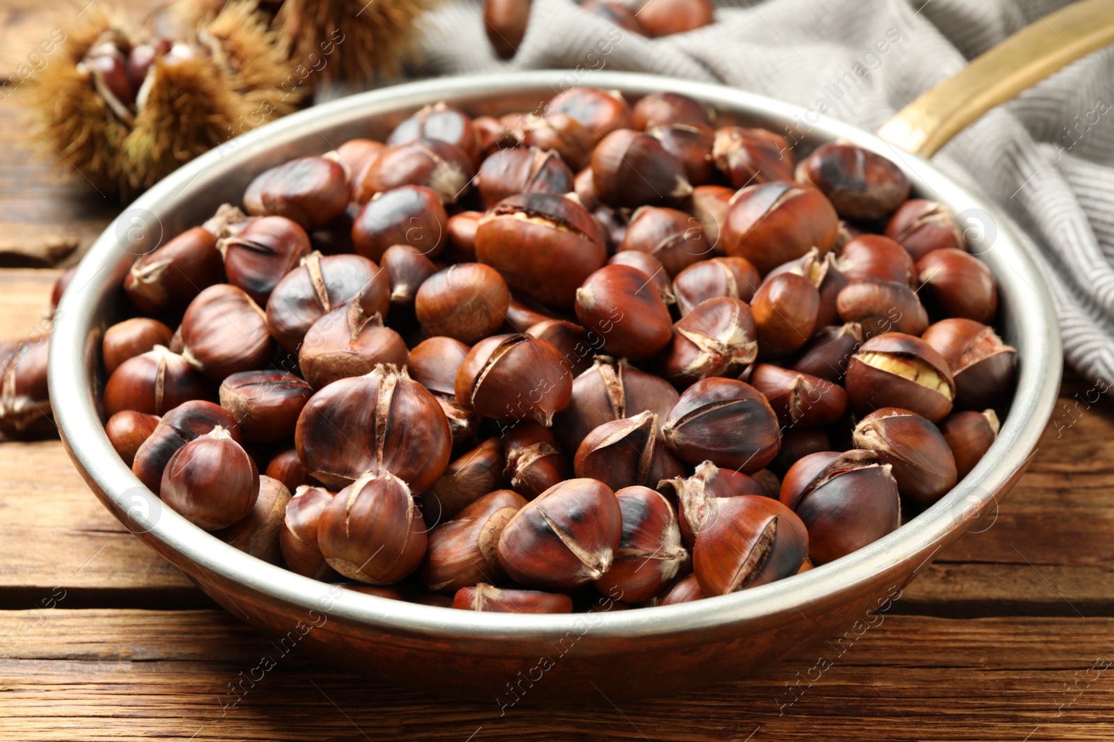 Photo of Delicious roasted edible chestnuts in frying pan on wooden table, closeup