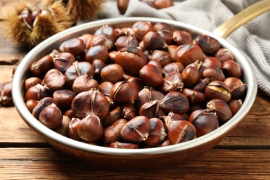 Photo of Delicious roasted edible chestnuts in frying pan on wooden table, closeup
