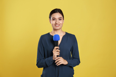 Young female journalist with microphone on yellow background