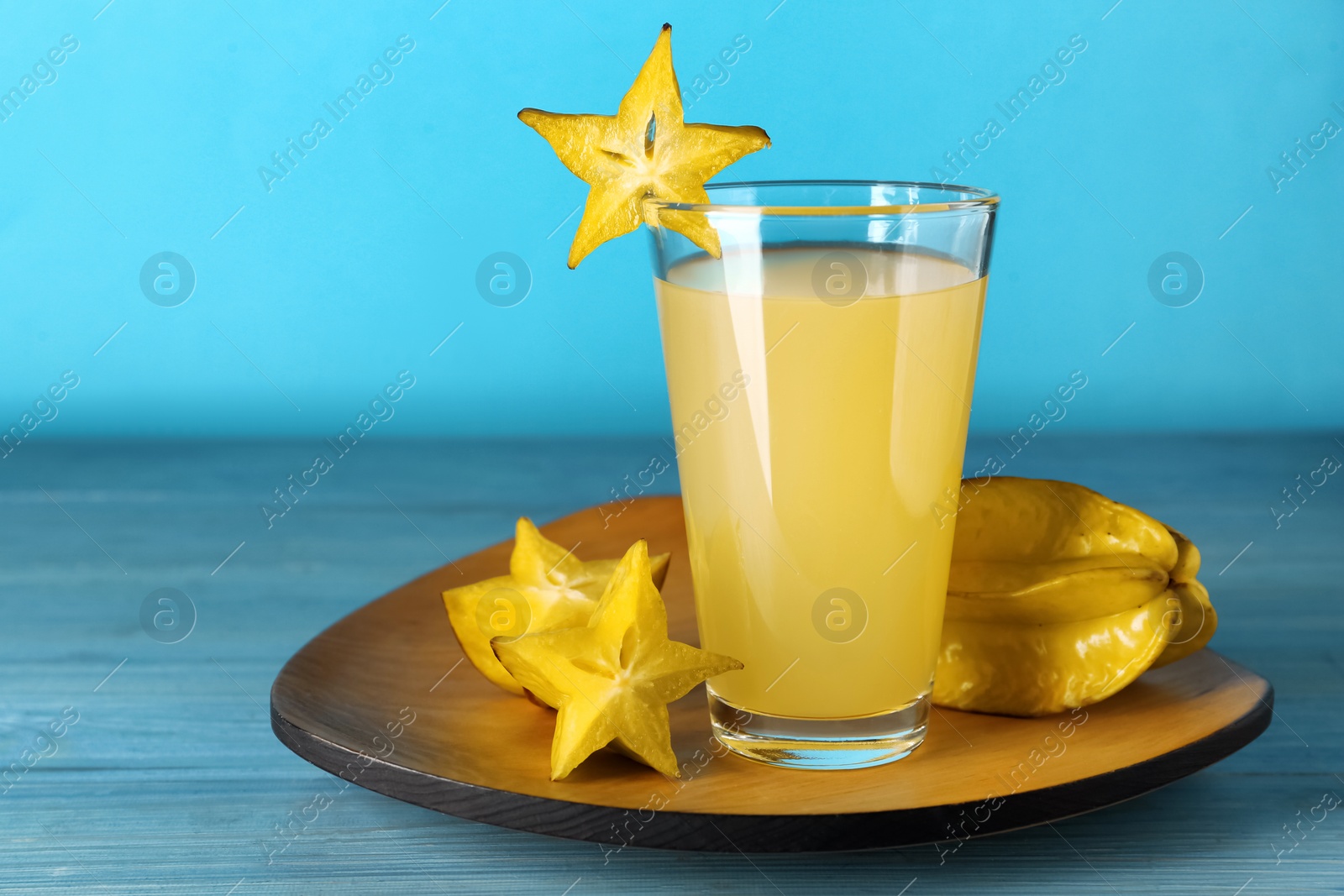 Photo of Delicious carambola juice and fresh fruits on light blue wooden table. Space for text