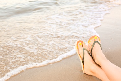 Photo of Closeup of woman with stylish flip flops on sand near sea, space for text. Beach accessories