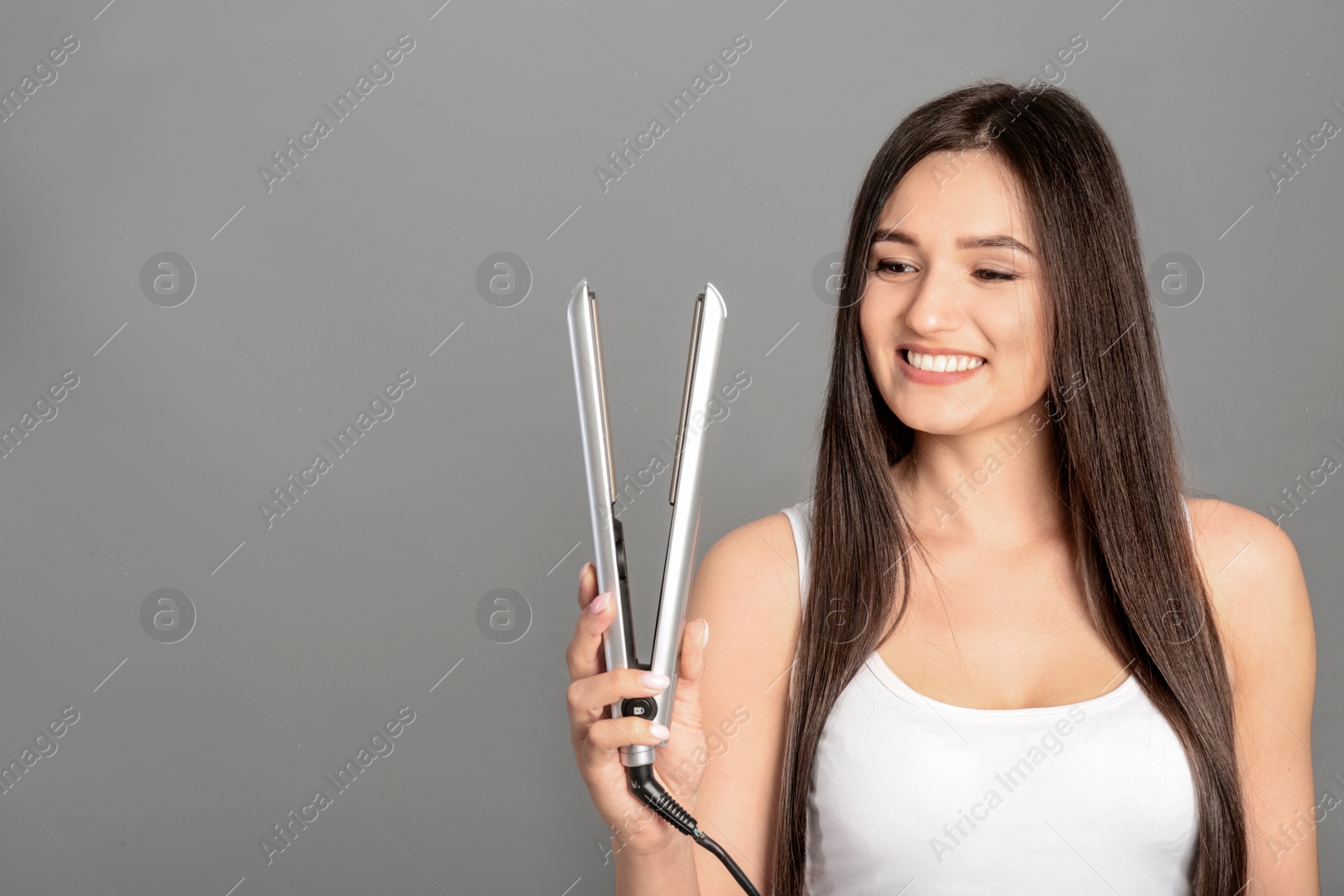 Photo of Young woman with modern hair iron on grey background, space for text