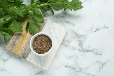 Bowl of celery seeds on white marble table, flat lay. Space for text