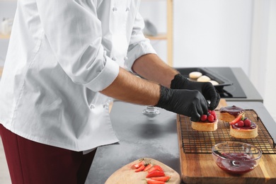 Male pastry chef preparing desserts at table in kitchen, closeup