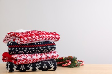 Stack of different Christmas sweaters and decor on table against light background. Space for text
