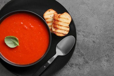 Photo of Delicious tomato cream soup in bowl and pieces of grilled bread served on dark textured table, top view. Space for text