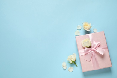 Photo of Pink gift box and beautiful flowers on light blue background, flat lay. Space for text