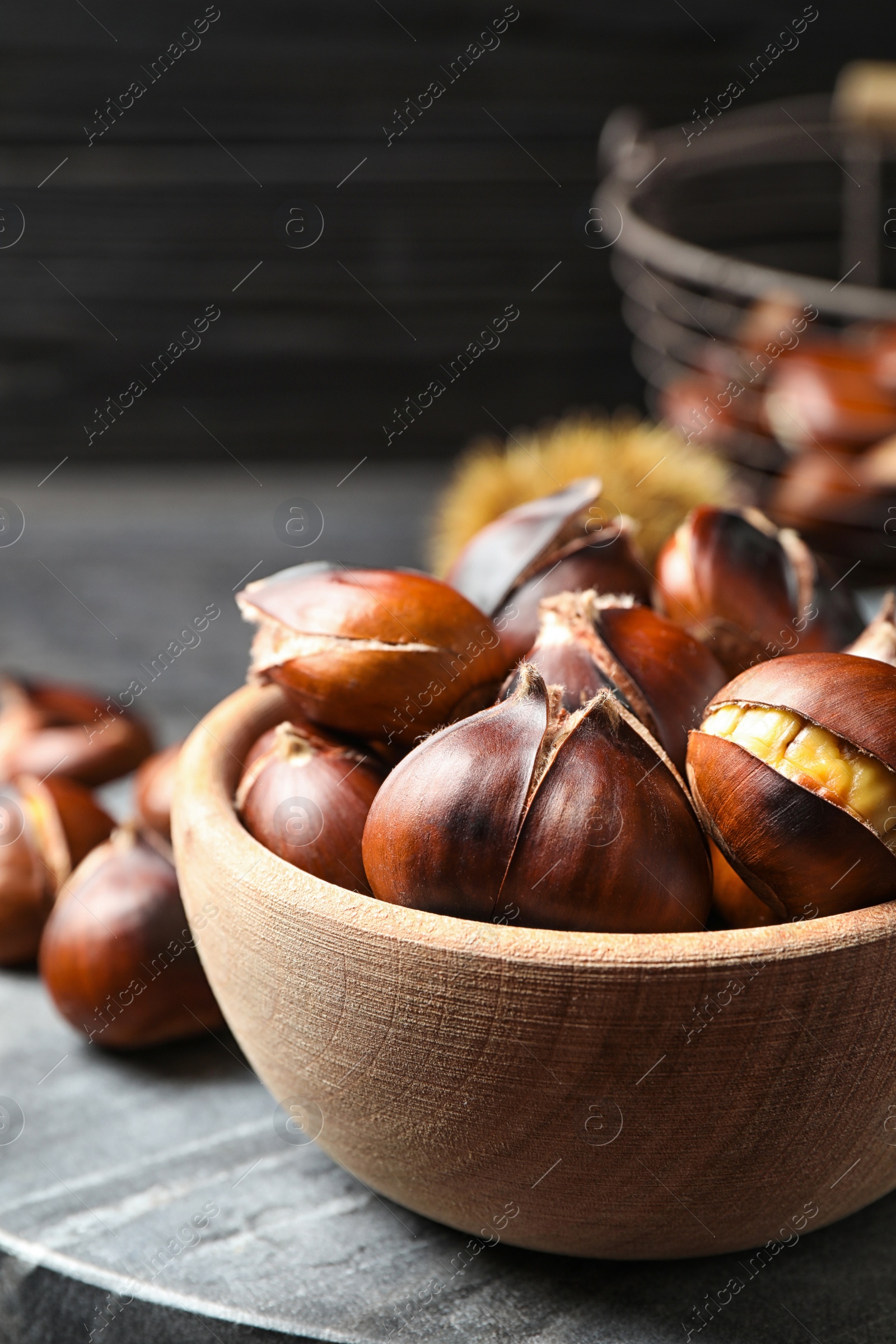Photo of Delicious roasted edible chestnuts in wooden bowl on grey marble board, closeup