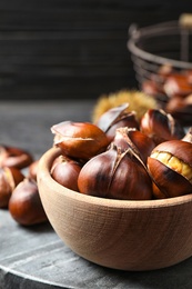 Delicious roasted edible chestnuts in wooden bowl on grey marble board, closeup