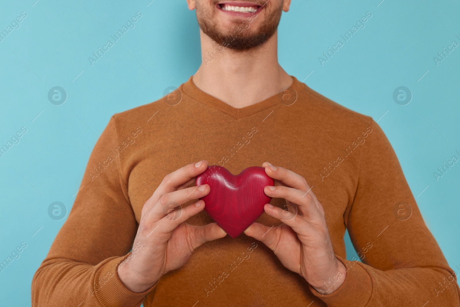 Photo of Happy volunteer holding red heart with hands on light blue background, closeup