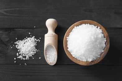 Organic salt in bowl and scoop on black wooden table, top view