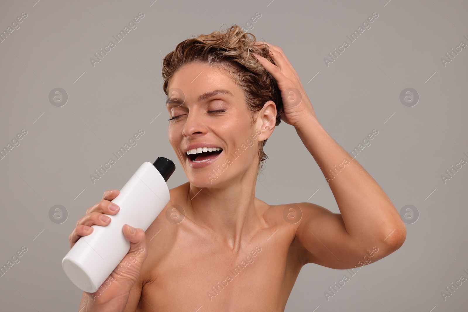 Photo of Portrait of happy woman with bottle singing while washing hair on light grey background