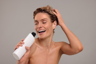 Portrait of happy woman with bottle singing while washing hair on light grey background