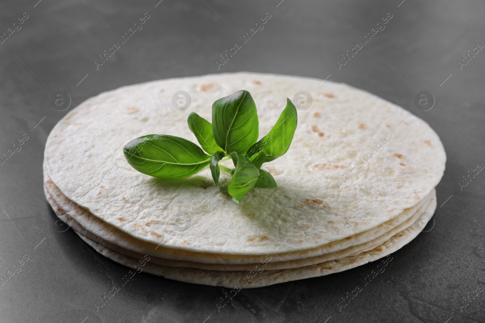Photo of Stack of tasty tortillas with basil leaves on grey table, closeup