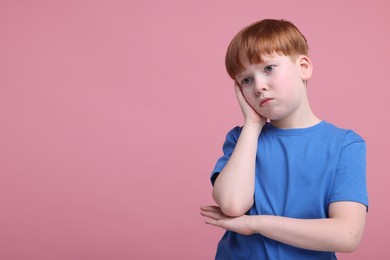 Portrait of sad little boy on pink background, space for text