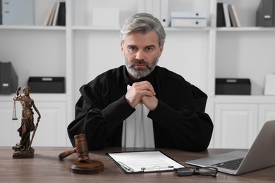 Judge with gavel, laptop and papers sitting at wooden table in office