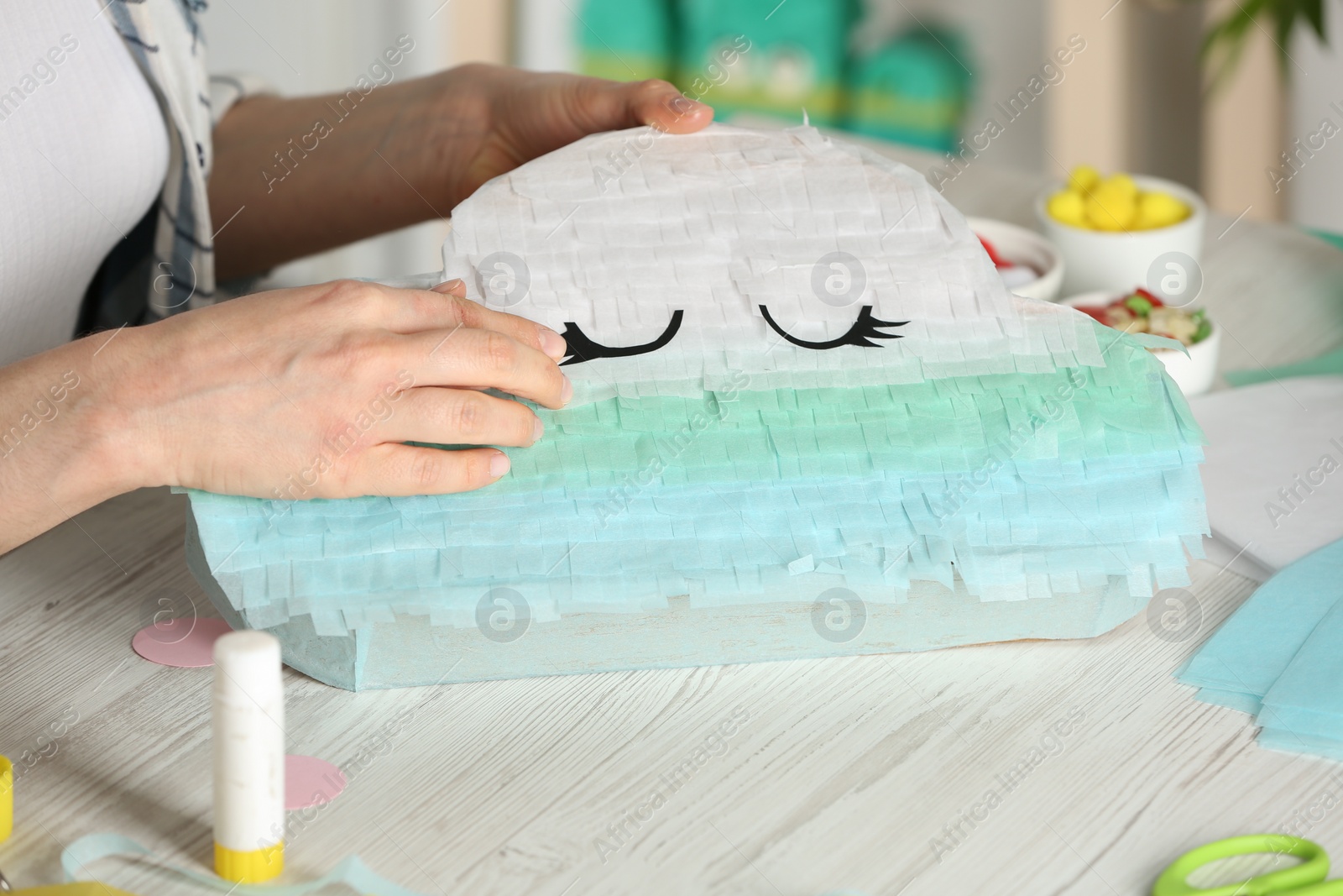 Photo of Woman decorating cardboard cloud at white wooden table, closeup. Pinata diy