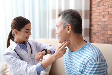 Doctor checking mature man's pulse with fingers indoors