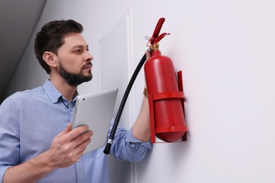 Photo of Man with tablet checking pressure and quality of fire extinguisher indoors. Space for text
