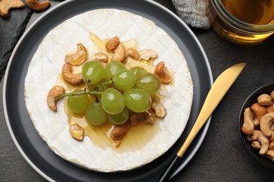 Photo of Brie cheese served with grape, cashew nuts and honey on dark grey table, flat lay