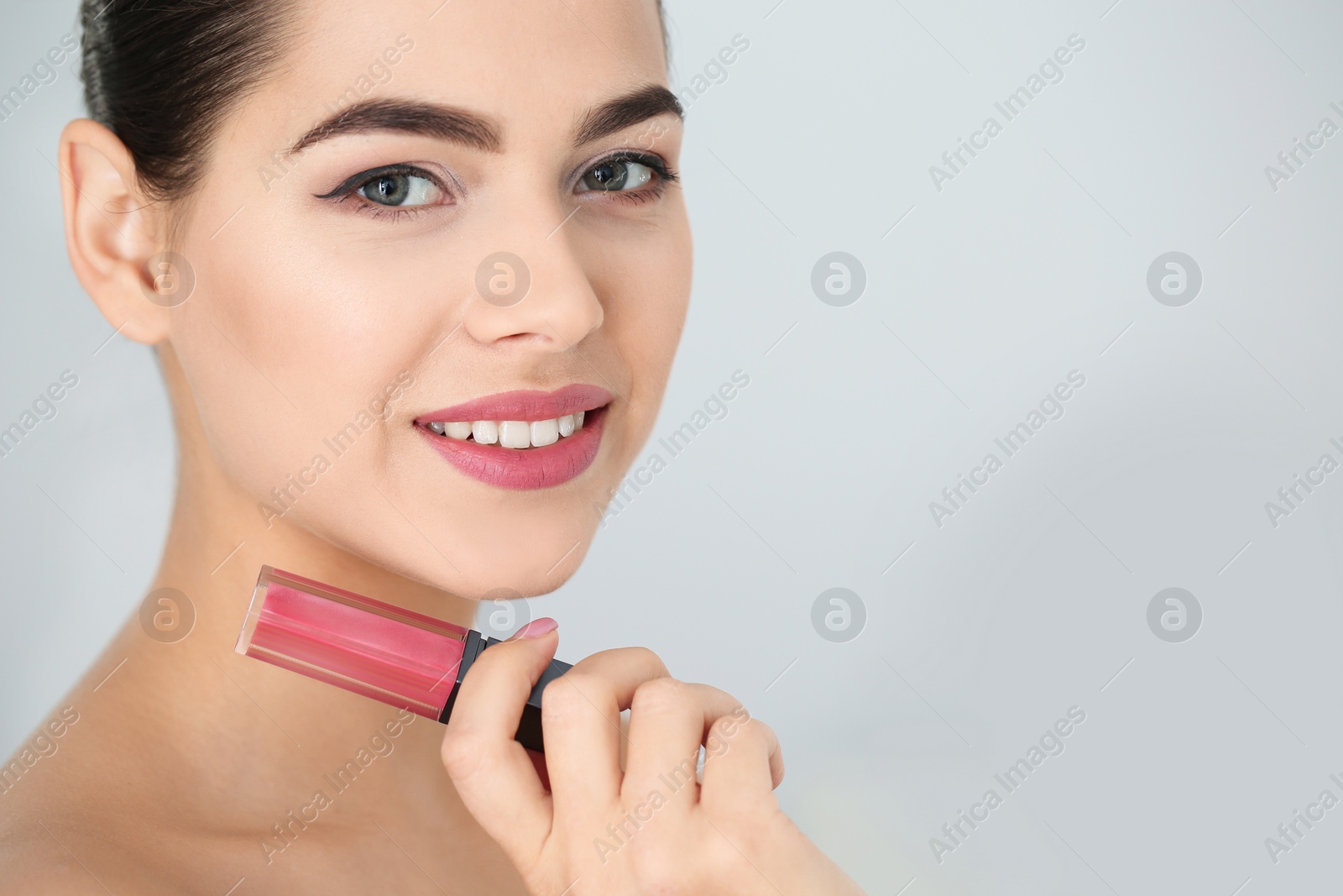 Photo of Young woman with liquid lipstick on light background. Space for text
