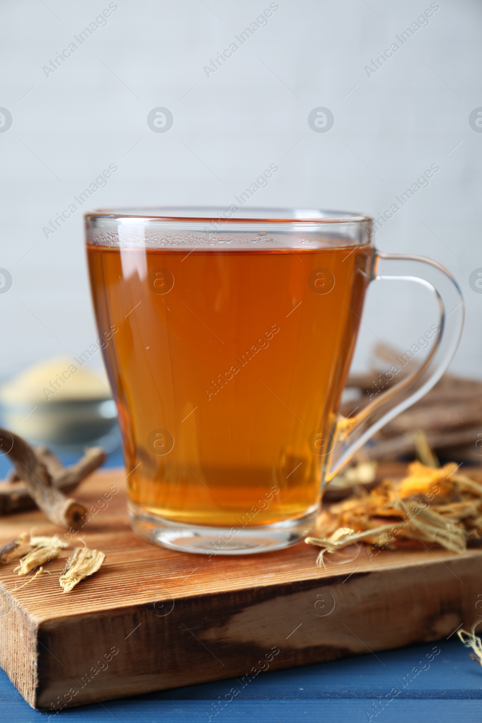 Photo of Aromatic licorice tea in cup and dried sticks of licorice root on blue wooden table, closeup