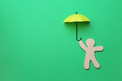 Mini umbrella and human figure on green background, flat lay. Space for text