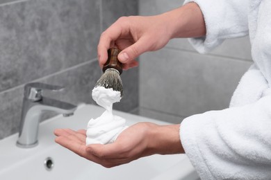 Photo of Man applying shaving foam onto brush in bathroom, closeup