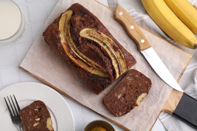 Delicious banana bread served on white tiled table, flat lay