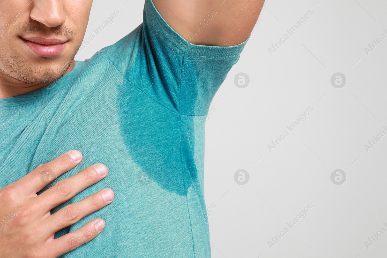 Photo of Young man with sweat stain on his clothes against light background, space for text. Using deodorant