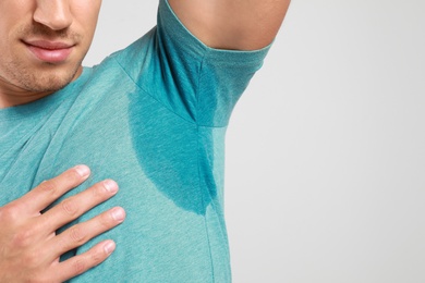 Young man with sweat stain on his clothes against light background, space for text. Using deodorant