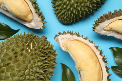 Photo of Fresh ripe durians and leaves on light blue background, flat lay