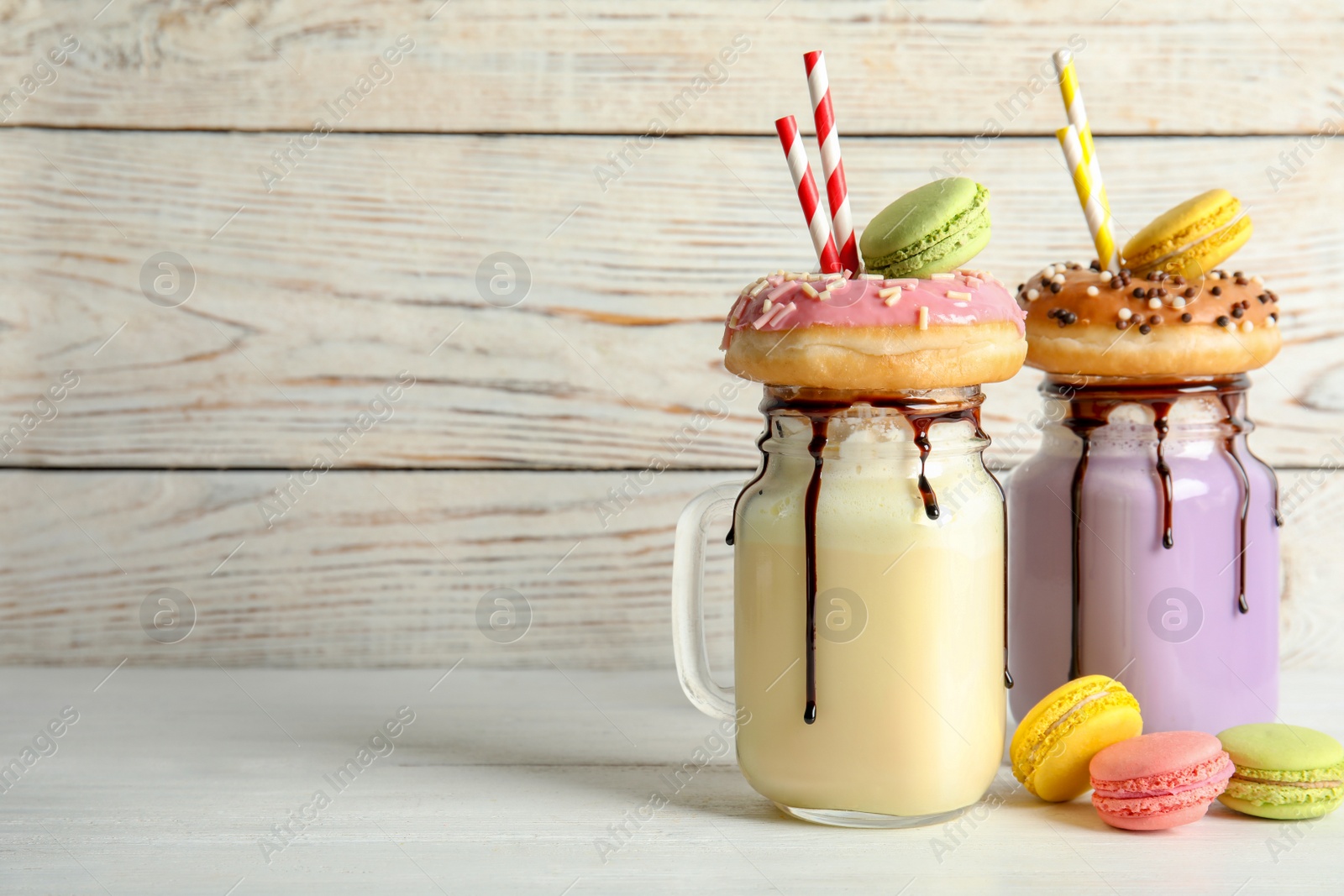 Photo of Mason jars with delicious milk shakes and macaroons on table. Space for text