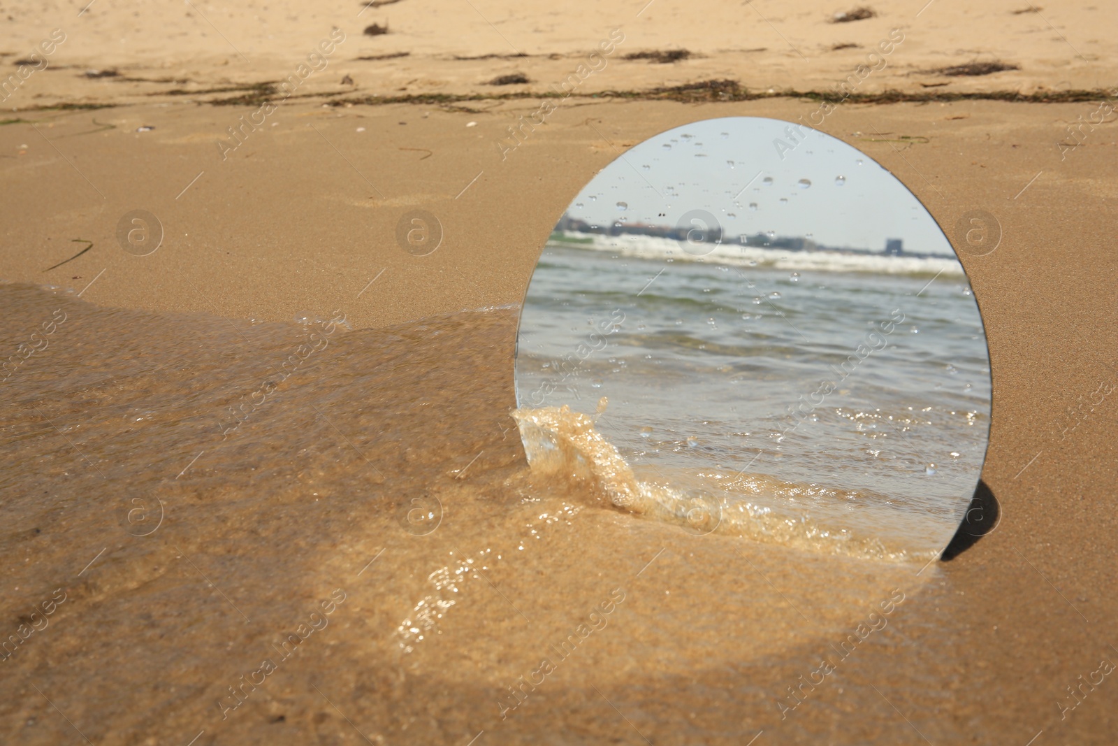 Photo of Round mirror reflecting sea on sandy beach