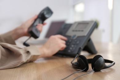 Photo of Woman using desktop telephone in office, focus on headset. Hotline service