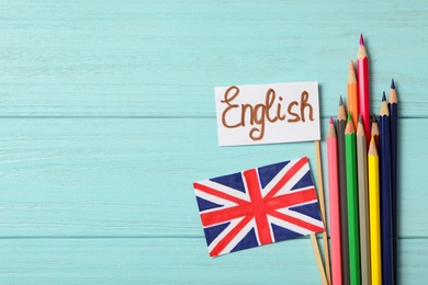 Photo of Word ENGLISH, UK flag and colorful pencils on light blue wooden background, flat lay. Space for text